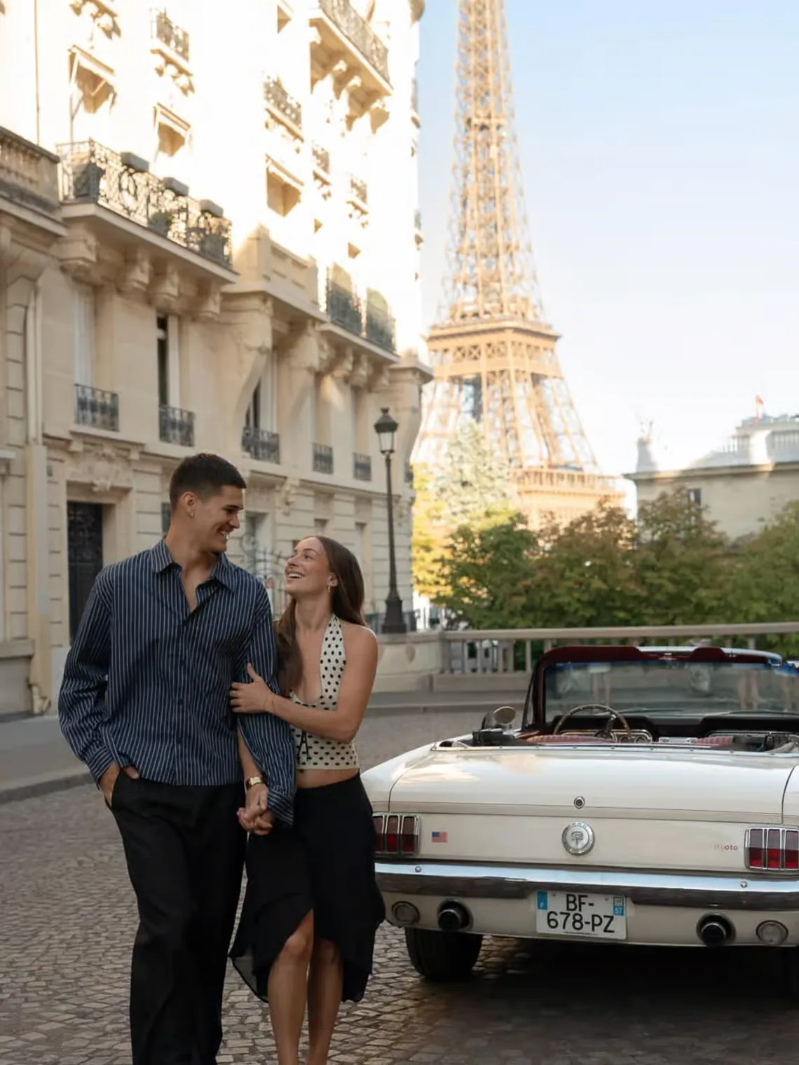 A couple sharing a smile beside the Mustang, with the Eiffel Tower above the street
