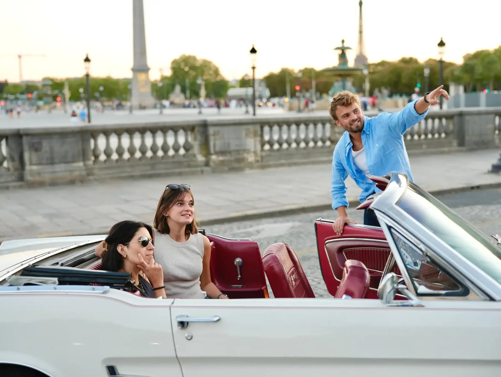 A driver-guide pointing out Paris sights to two guests seated in the open Mustang